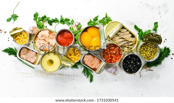 Food background\
in tin cans. Canned vegetables, beans, fish and fruits on a white\
wooden background. Top\
view.