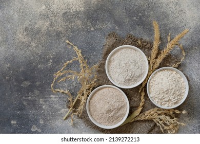Food and baking ingredient. Wheat flour coarse from whole wheat grains, wheat bran and wheat flour over gray stone background. Top view flat lay. Copy space. 