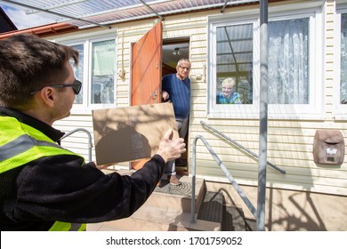 food bank delivery. A volunteer / soldier bringst food for senior citizens. The volunteer in a medical mask and gloves passes a bag of products to an elderly couple in masks on the steps. Coronavirus. - Powered by Shutterstock