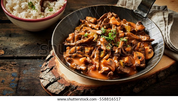 Food banner of meat cut into strips.\
Pan with goulash stroganoff meal on rustic wooden\
plate