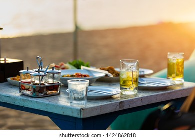 Food And Beverage On The Table At Beach Bar For Dinning Party On The Beach And Have Sunset Light And Blurry Sea Background.