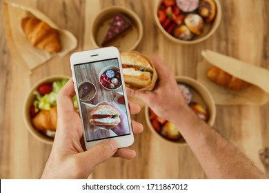 Food Blogger Reviewing Takeout Food, Capturing Video On His Phone. Italian Panini Sandwich, French Croissant With Salmon & Chocolate Cheesecake. Close Up, Top View, Pov, Copy Space, Wooden Background.