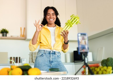 Food Blogging. Happy Black Lady Shooting On Phone Camera In Kitchen, Cooking And Recording Video Content For Social Media. African American Woman Showing Selera To Smartphone On Tripod