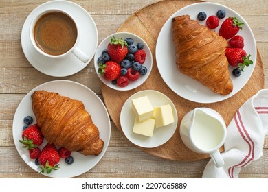 El concepto de restauración y desayuno, croissant recién horneado con bayas y taza de café, fondo de madera, vista superior