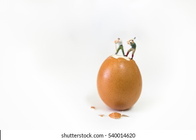 Food, Business Concept. Two Miniature Figures Worker Stand And Woking On Brown Egg To Break Eggshell - On White Background