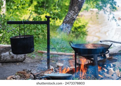 Food camping concept. Cooking over an open fire outdoors during a summer picnic.Traveling, tourism, picnic, cooking at the stake in a cauldron, fire and smoke. - Powered by Shutterstock