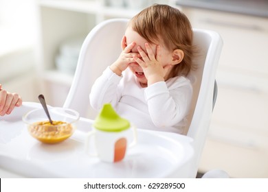 food, child, feeding and people concept - baby with spoon sitting in highchair and eating puree from at home kitchen - Powered by Shutterstock