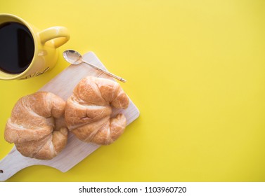 food concept, flat lay of croissant and coffee on yellow background with copy space.