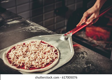 Food concept. Preparing traditional italian pizza. Chef holds long irob shovel for pizza, baking dough with pasta and cheese in a professional oven. Only hands close up