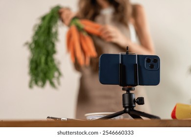 Food content creator setting up smartphone on tripod to film healthy cooking vlog with fresh vegetables and carrots - Powered by Shutterstock