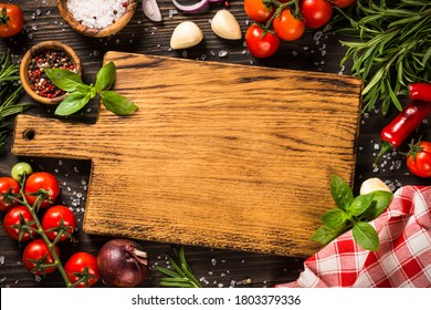 Food cooking background with cutting board, spices, herbs and vegetables at wooden kitchen table. Top view with copy space.
