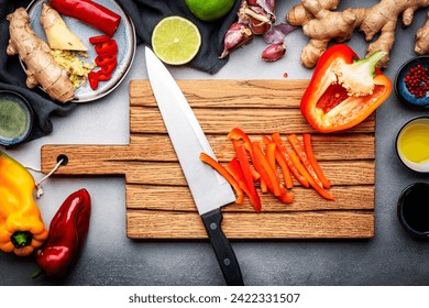 Food and cooking background. Wooden cutting board with chopped paprika and chef knife. Zucchini, raw vegetables, spices and ingredients for cooking vegan Asian dishes with ginger, garlic, soy sauce - Powered by Shutterstock