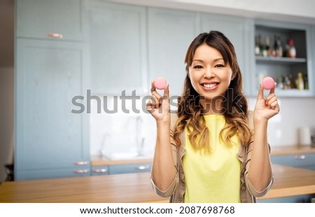 food, cooking and baking concept - happy asian young woman with macarons at home over kitchen background