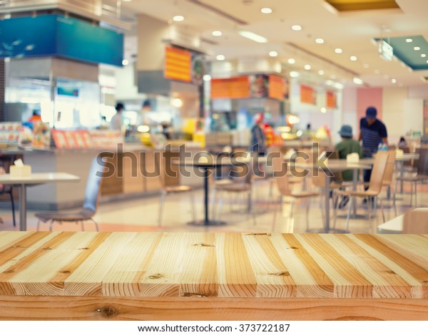 Food court or food center in shopping mall.\
Interior consist of table, restaurant, coffee shop. Busy with \
people to buy food, sitting, eating. Wood table top for product\
display or blurred\
background