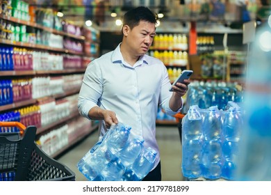 Food Crisis, Drinking Water Shortage, Asian Man In Supermarket Buying Bottled Water, Nervous And Sad Reading Bad News On Phone