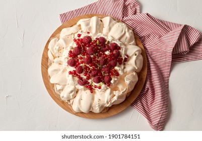 Food, Culinary, Baking And Cooking Concept - Close Up Of Pavlova Meringue Cake Decorated With Red Berries On Wooden Serving Board And Kitchen Towel