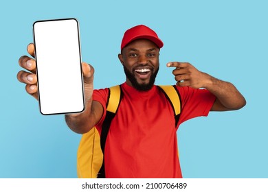 Food Delivery App. Black Courier Guy With Thermo Backpack Pointing At Blank Smartphone With White Screen, African Deliveryman In Uniform Recommending Mobile Application For Online Order, Mockup