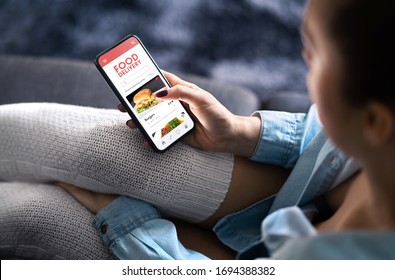 App für die Lebensmittelzustellung auf dem Handy. Bestellung im Restaurant online. Frauen mit Smartphone, um mitzunehmen Mittagessen nach Hause geliefert. Schneller Kurierdienst. Burger-Menü, die im Handybildschirm angezeigt wird.
