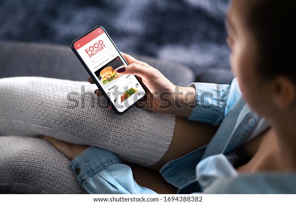 Food\
delivery app in mobile phone. Restaurant order online. Woman using\
smartphone to get take away lunch home delivered. Fast courier\
service. Burger menu mock up in cellphone\
screen.