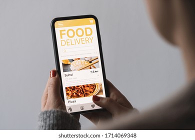 Food Delivery App On A Mobile Phone. Restaurant Order Online. Woman Using Smartphone To Get Take Away Lunch Home Delivered. Fast Courier Service. Suhsi And Pizza Menu Mock Up In Cellphone Screen.