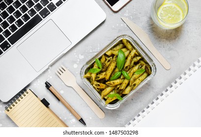 Food delivery concept. Lunch box with pasta penne with pesto and basil, glass of water with lemon, eco fork and knife  on grey office table. Lunch at the office. Top view , flat lay food, Takeaway - Powered by Shutterstock