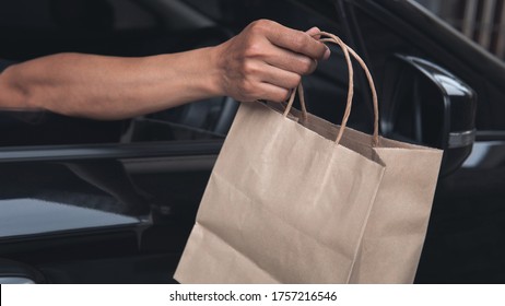 Food Delivery Man Driver’s Hand Holding Environmentally Friendly Craft Brown Paper Bag Out Of A Black Car Window Meeting Social Distancing Requirements And Supporting Small Business