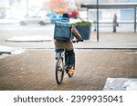 Food delivery man riding bicycle on snowy city street with large black backpack. Delivery boy on bike with thermal bag deliver pizza from restaurants during snow storm
