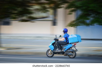 Food delivery moto scooter driver is on his way to deliver food. Courier on motor scooter delivering food. Delivery man in helmet, face mask, gloves ride scooter. Express food delivery, shop online - Shutterstock ID 2228663765