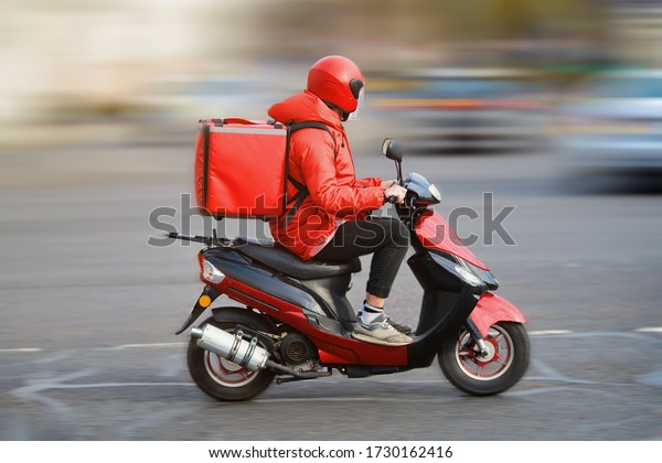 Food delivery moto scooter\
driver with red backpack behind back is on his way to deliver food.\
Courier on scooter delivering food. Quick shipping of goods to\
customers