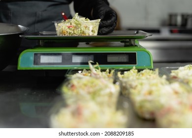 Food Delivery In The Restaurant. Close-up Of A Chef's Hand In Gloves Weighing A Portion Of Salad On An Electronic Scale. Small Business. Takeout Food. Copy Space.