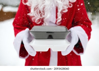 Food Delivery Service Containers In Hands Of Santa Claus Outdoor In Snow. Christmas Eve Promotion. Ready-made Hot Order, Disposable Plastic Box. New Year Holidays Catering. Copy Space, Mock Up