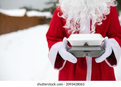 Food Delivery Service Containers In Hands Of Santa Claus Outdoor In Snow. Christmas Eve Promotion. Ready-made Hot Order, Disposable Plastic Box. New Year Holidays Catering. Copy Space, Mock Up