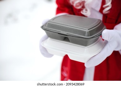 Food Delivery Service Containers In Hands Of Santa Claus Outdoor In Snow. Christmas Eve Promotion. Ready-made Hot Order, Disposable Plastic Box. New Year Holidays Catering. Copy Space, Mock Up