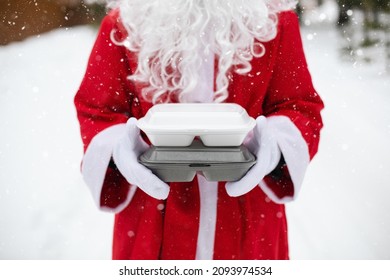 Food Delivery Service Containers In Hands Of Santa Claus Outdoor In Snow. Christmas Eve Promotion. Ready-made Hot Order, Disposable Plastic Box. New Year Holidays Catering. Copy Space, Mock Up