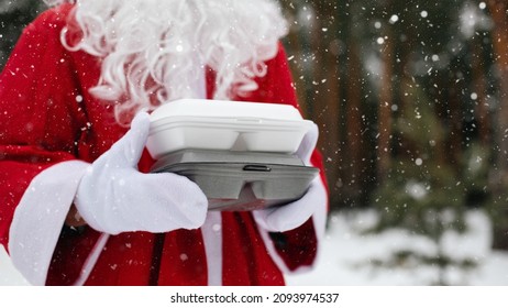 Food Delivery Service Containers In Hands Of Santa Claus Outdoor In Snow. Christmas Eve Promotion. Ready-made Hot Order, Disposable Plastic Box. New Year Holidays Catering. Copy Space, Mock Up