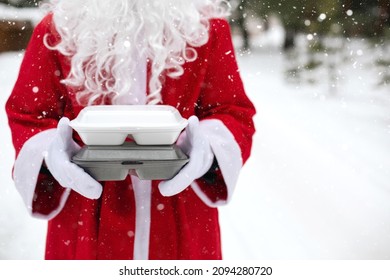 Food Delivery Service Containers In Hands Of Santa Claus Outdoor In Snow. Christmas Eve Promotion. Ready-made Hot Order, Disposable Plastic Box. New Year Holidays Catering. Copy Space, Mock Up