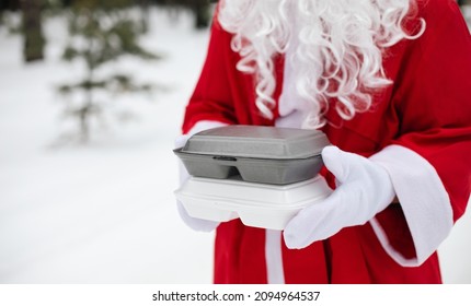 Food Delivery Service Containers In Hands Of Santa Claus Outdoor In Snow. Christmas Eve Promotion. Ready-made Hot Order, Disposable Plastic Box. New Year Holidays Catering. Copy Space, Mock Up