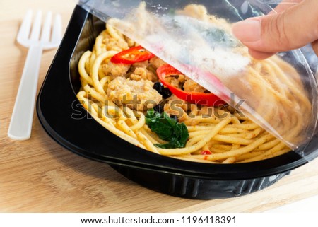 Food Delivery service: Woman hands holding open cling wrap and take out food in plastic boxes on wood background. concept online order take away food ready for home delivery.