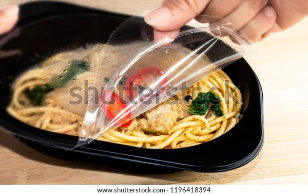 Food Delivery service:\
Woman hands holding open cling wrap and take out food in plastic\
boxes on wood background. concept online order take away food ready\
for home delivery.