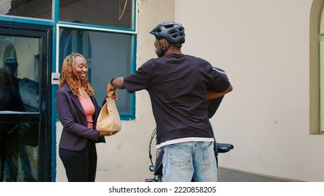 Food Delivery Service Worker Delivering Lunch Meal To Woman, Man Giving Client Paper Bag With Restaurant Food. Smiling African American Customer Taking Fastfood Takeaway Meal Outdoors.