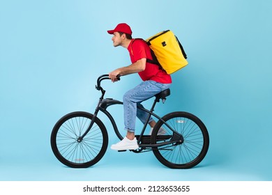 Food Delivery. Side View Of Courier Guy Riding Bike With Yellow Backpack Bag Delivering Meal From Takeaway Cafe Or Restaurant Over Blue Background, Studio Shot. Deliveryman Service Concept - Shutterstock ID 2123653655