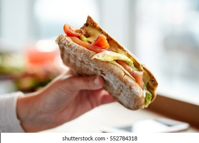 food, dinner, eating and people concept - hand with salmon panini sandwich with tomatoes and cheese at restaurant