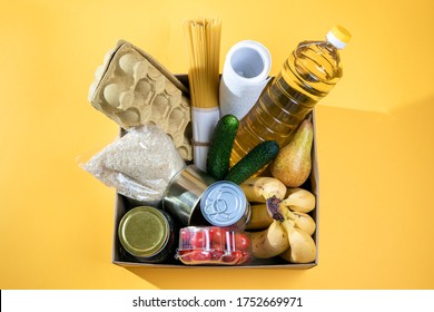 Food Donation In A Cardboard Box On  Yellow Background, Place Of Copy. Contactless Delivery Food. Grocery Box With  Food Products Top View, Volunteering And Self-isolation Help