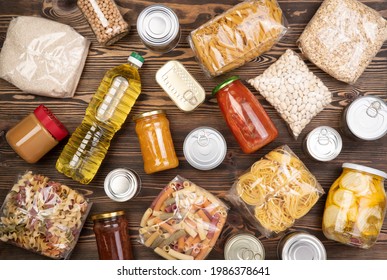 Food Donations Such As Pasta, Rice, Oil, Peanut Butter, Canned Food, Jam And Other On Brown Wooden Table , Top View