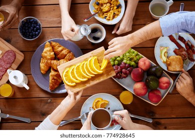 Food, Eating And Family Concept - Group Of People Having Breakfast And Sharing Orange At Table