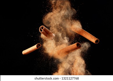 Food explosion with cinnamon sticks and powder, on black background.
