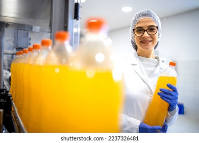 Food factory female supervisor standing in bottling plant and holding orange juice bottle. - Powered by Shutterstock