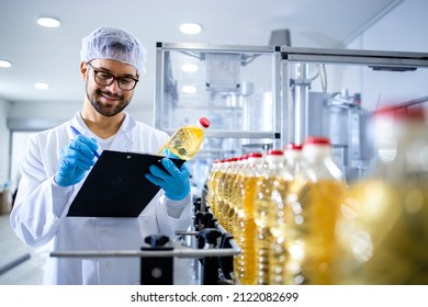 Food factory worker inspecting product quality and controlling production of refined edible bottled oil.