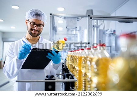 Food factory worker inspecting product quality and controlling production of refined edible bottled oil.