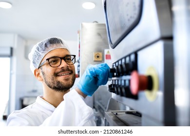 Food factory worker in sterile uniform and hairnet operating industrial production machine.